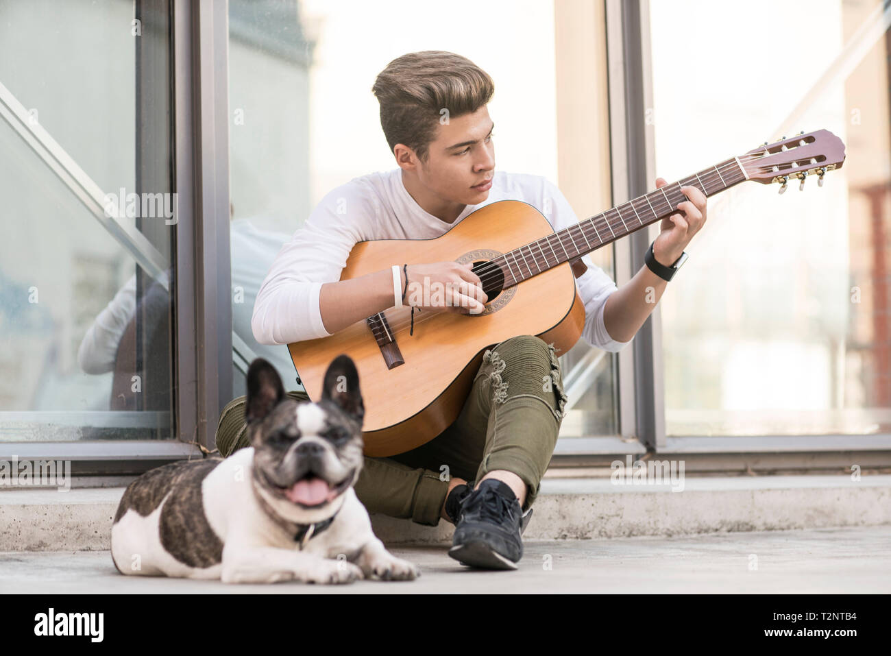 Teenage refugee boy playing guitar on pavement with dog Stock Photo