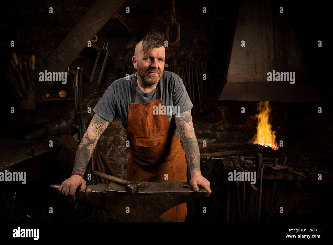Mature male blacksmith leaning against anvil in workshop, portrait Stock Photo