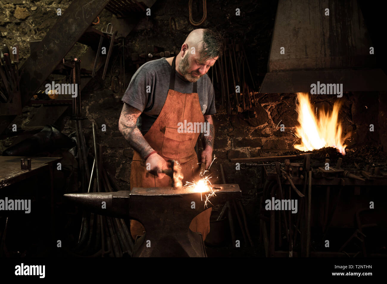 Mature male blacksmith hammering metal on anvil in workshop Stock Photo