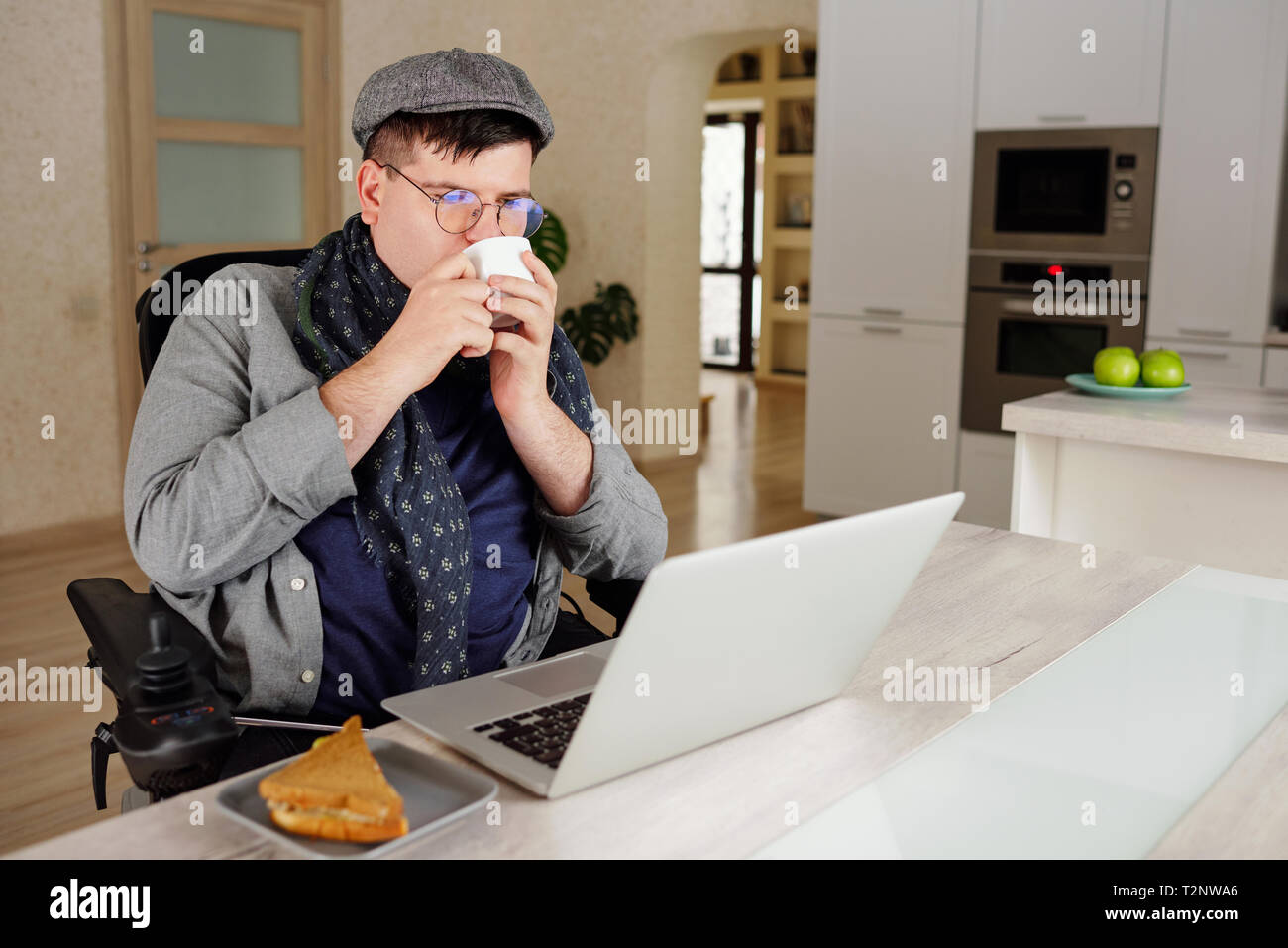 Physically impaired man drinking and working on laptop at home Stock Photo