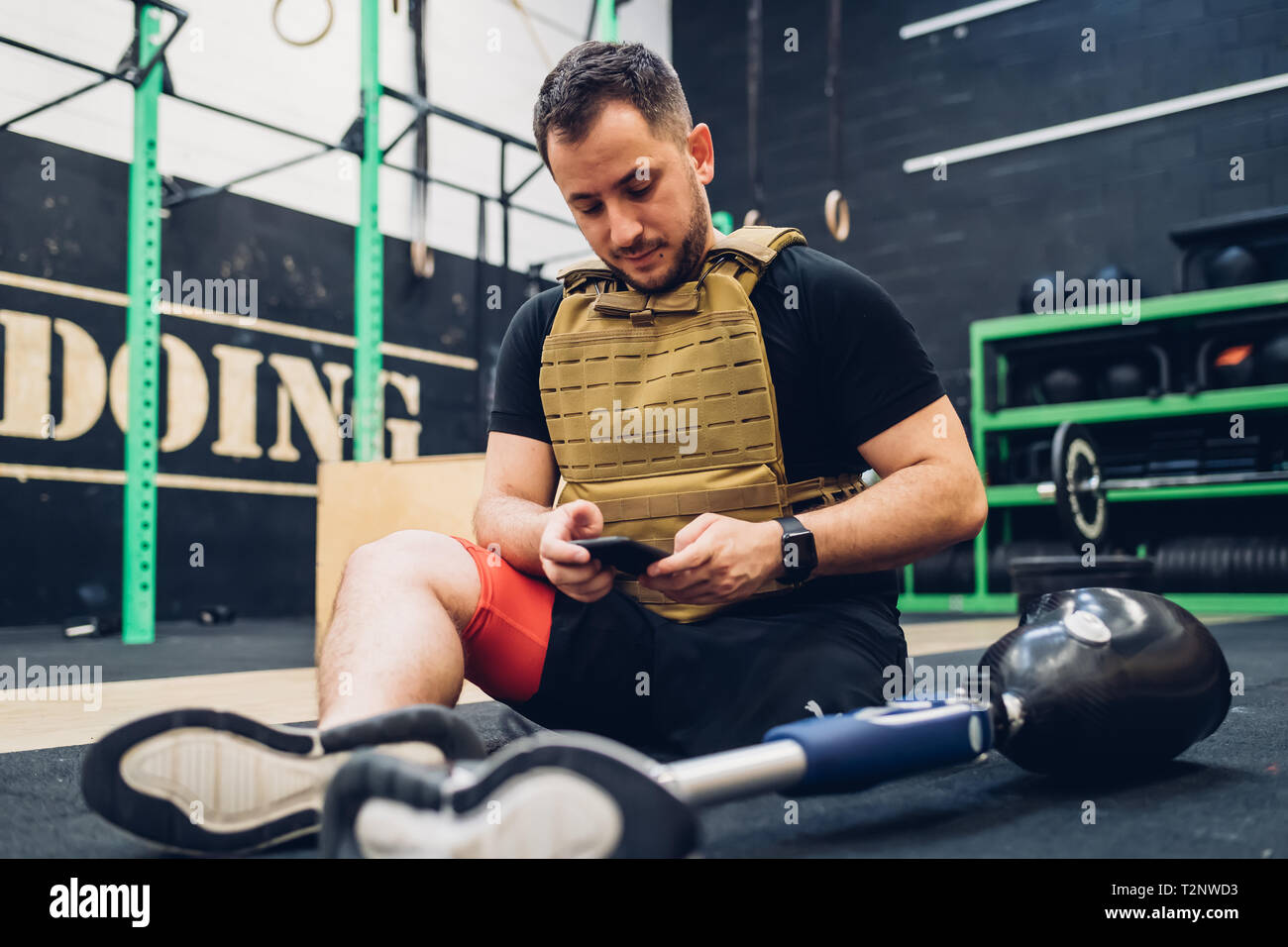 Man with prosthetic leg sitting on gym floor texting Stock Photo
