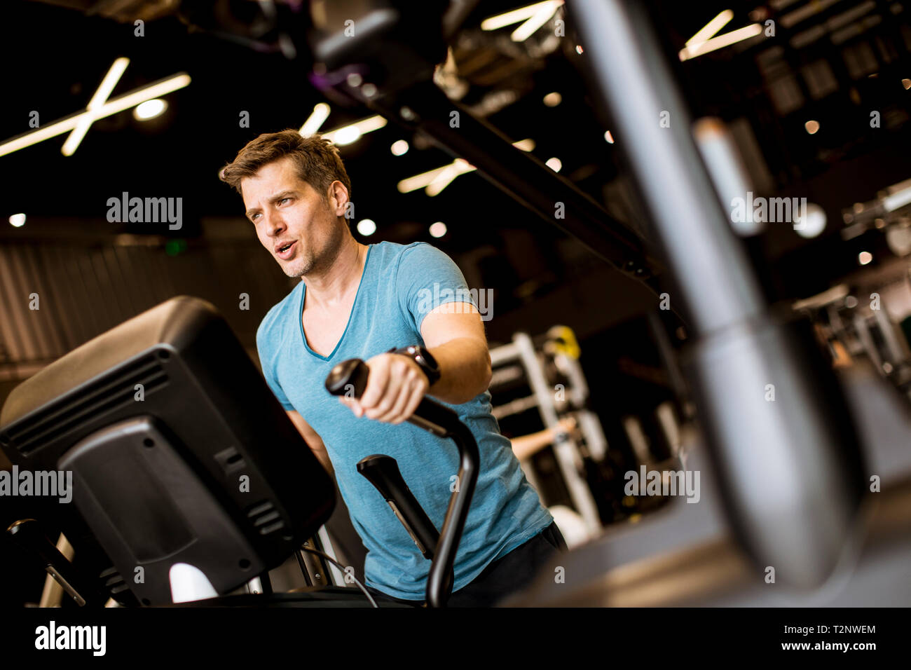 Young man doing exercise on elliptical cross trainer in sport fitness gym club Stock Photo