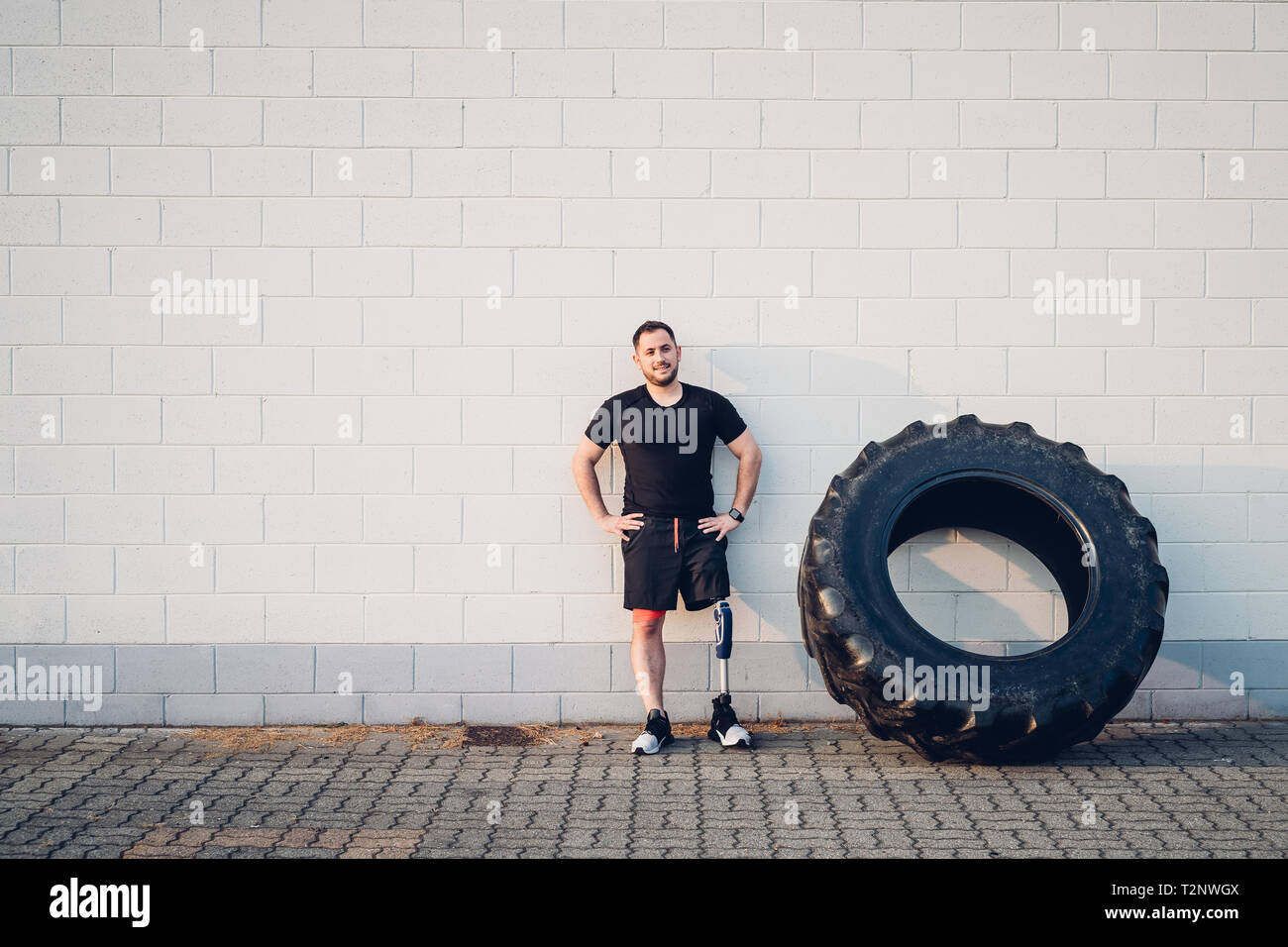 Man with prosthetic leg leaning on wall beside training tyre Stock Photo