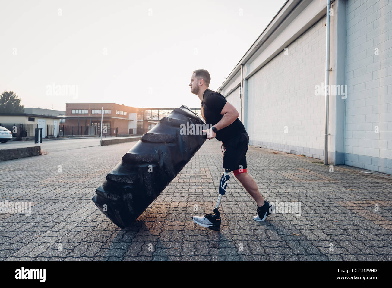 Man with prosthetic leg weight training with giant tyre Stock Photo