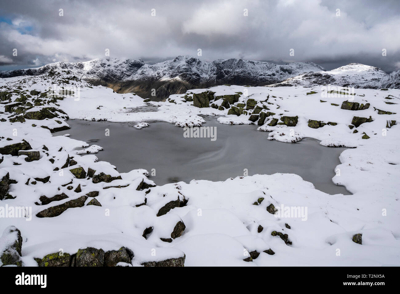 Icy tarn on the summit of Crinkle Crags, looking towards the Scafell Range, Lake District, Cumbria Stock Photo