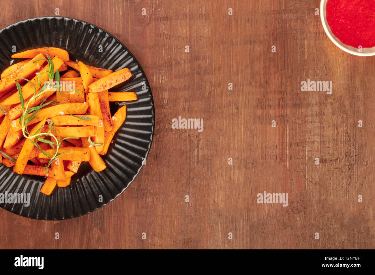 Roasted sweet potato fries with rosemary and a tomato sauce, shot from the top on a dark rustic wooden background, forming a frame for copy space Stock Photo