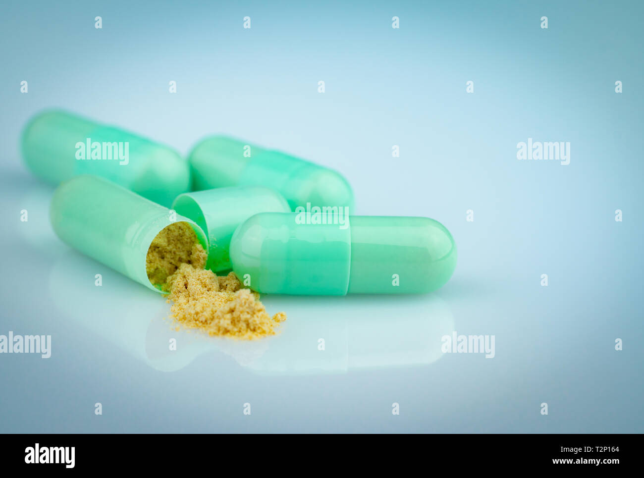 Group of green capsule and open one capsule to show yellow powder of herbal medicine on gradient background. Pharmaceutical product. Green capsule Stock Photo