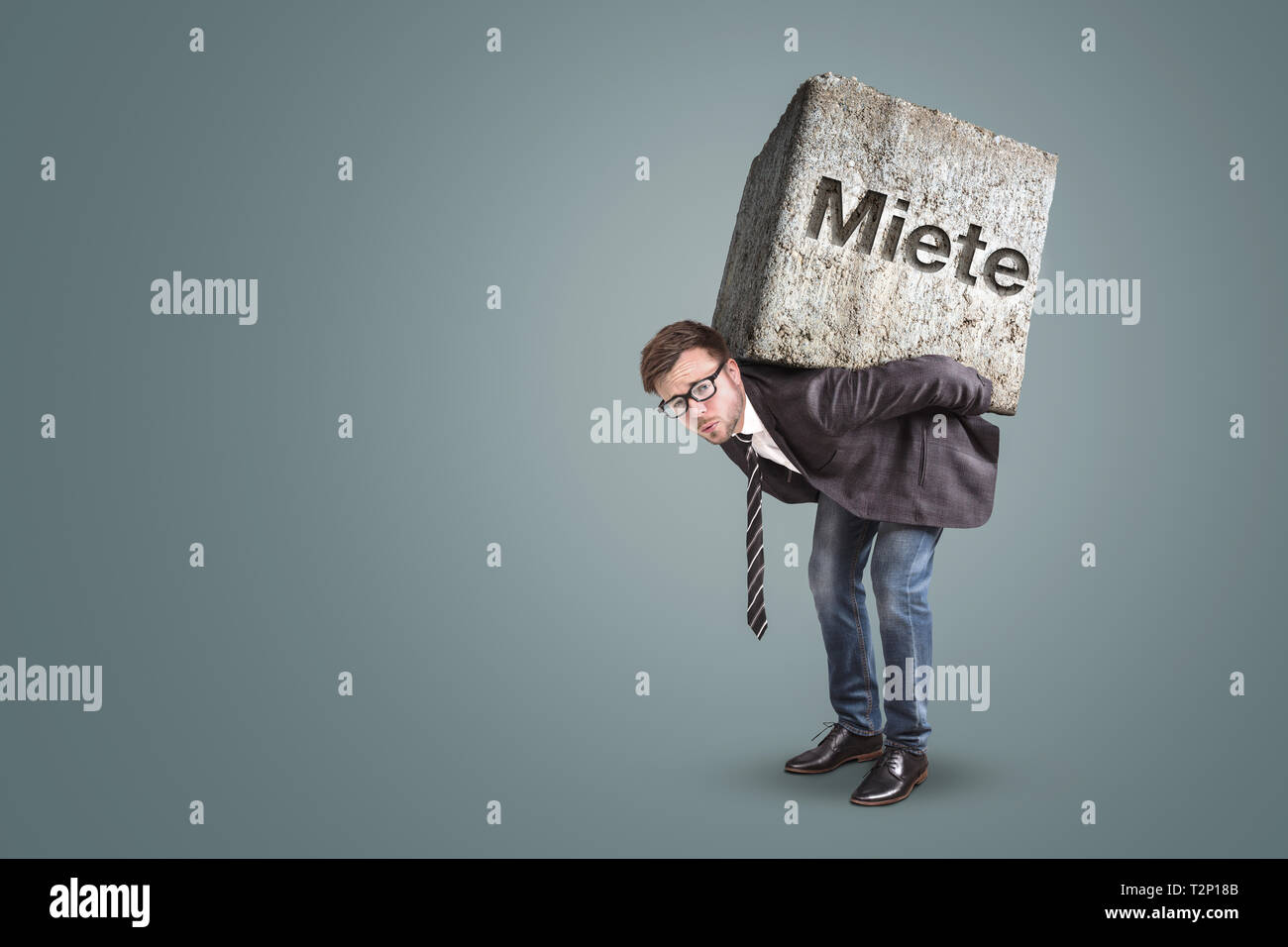 Conceptual image of a man carrying a heavy stone with the German word “Miete” written on it. Stock Photo