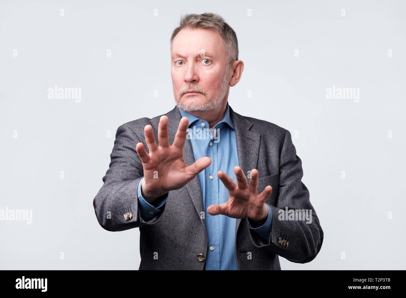 Mature european man in suit showing refusal gesture. It is not for me, leave me in piece, has angry expression. Studio shoot Stock Photo