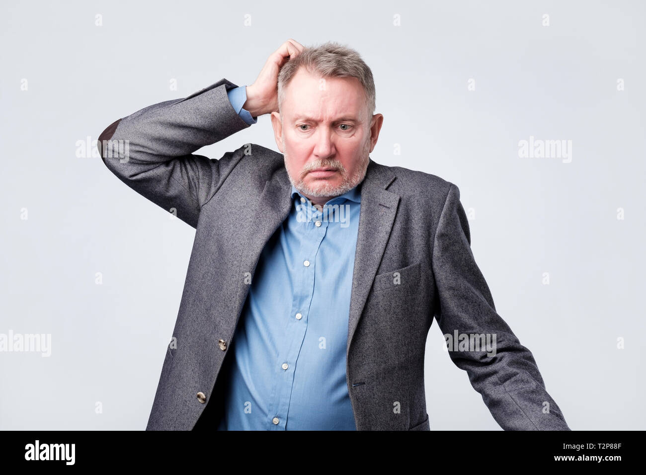 Pensive senior man in suit scratching his head having doubts about his job. Stock Photo