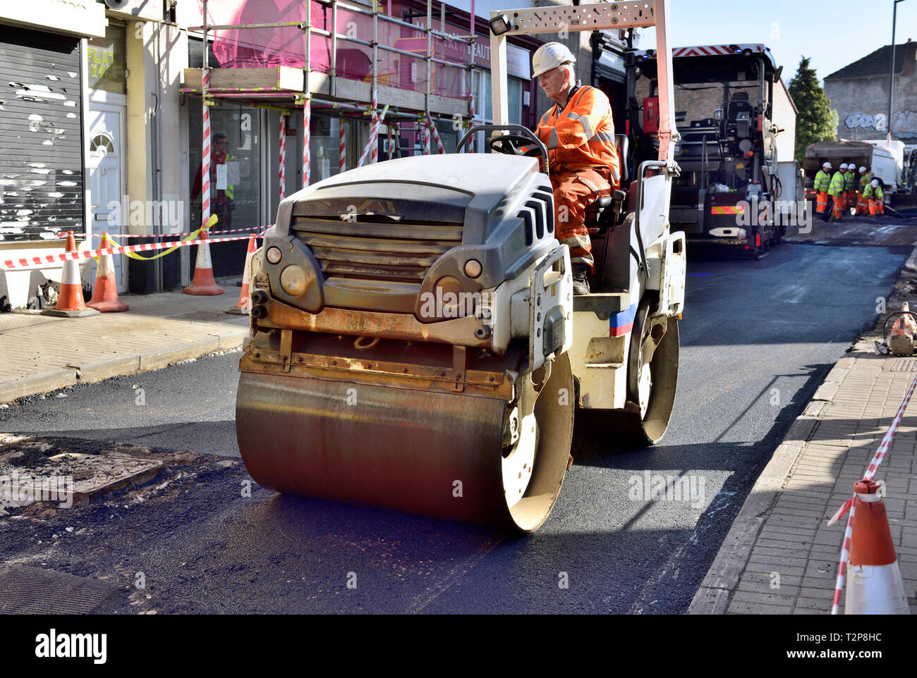 Road roller working on refurbishment of city street with fresh tarmac, England, UK Stock Photo