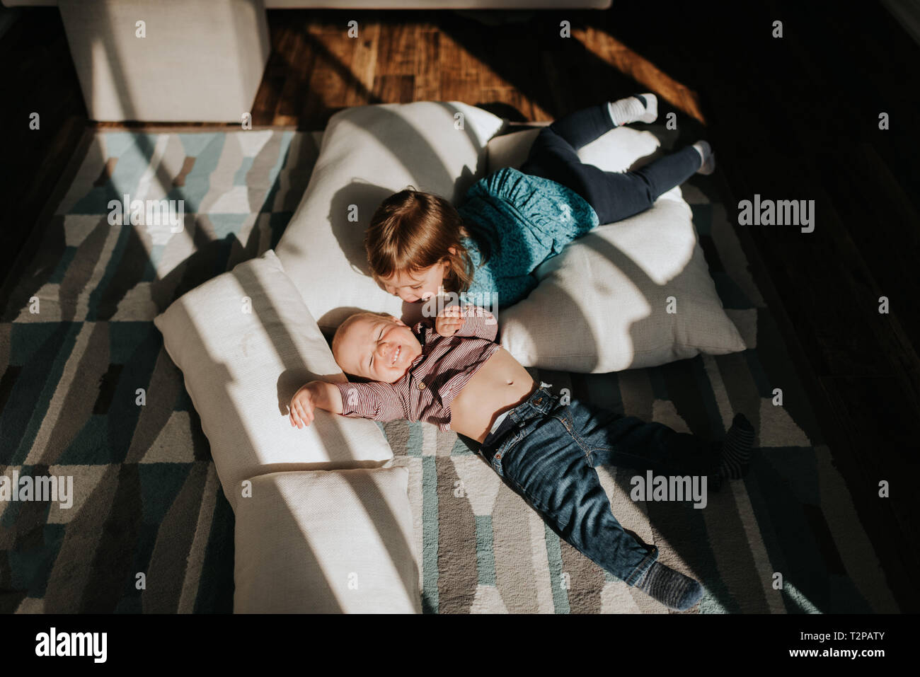 Baby boy and toddler sister lying on cushions on living room floor, overhead view Stock Photo