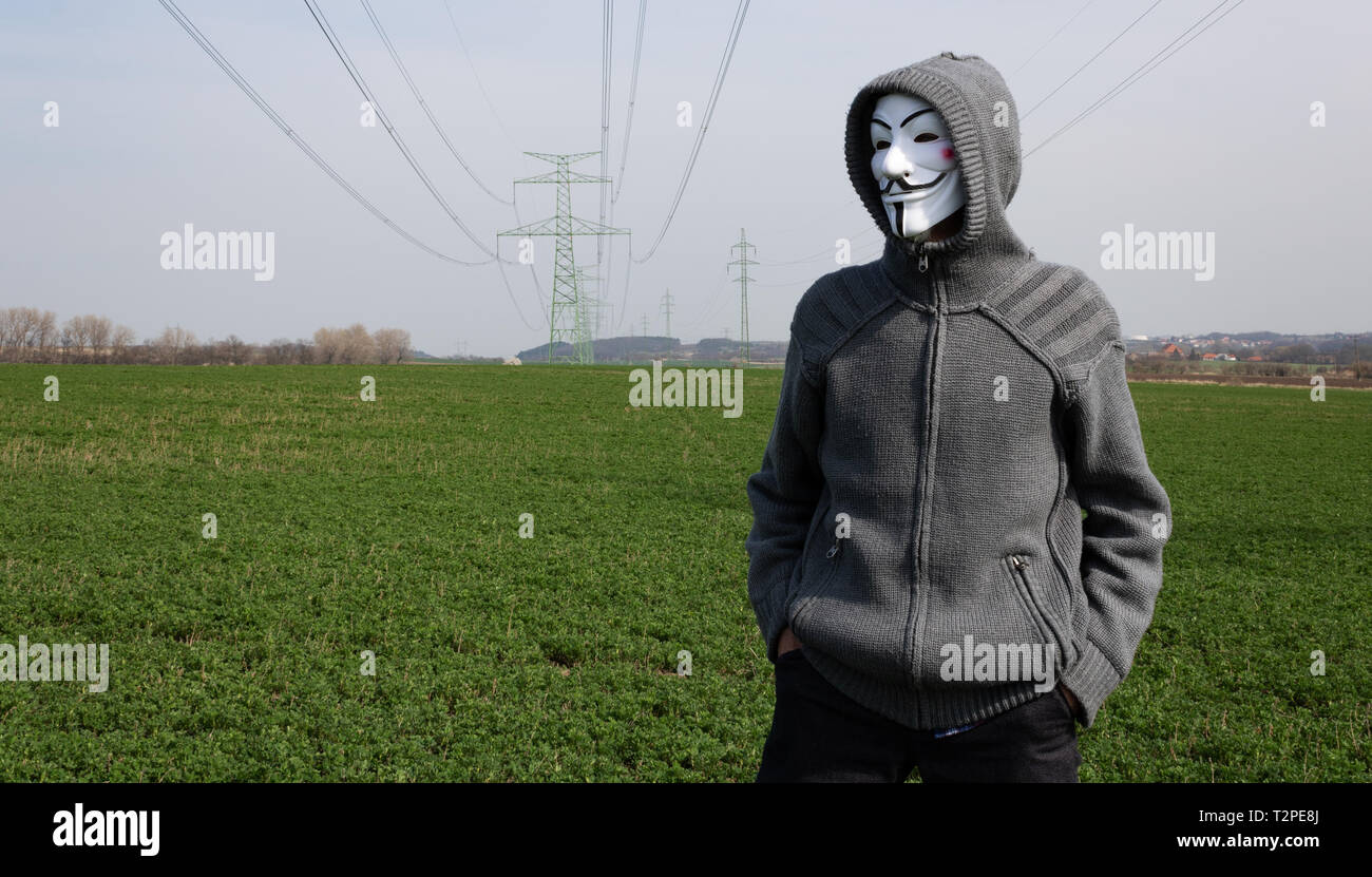 Velvary, CZECH REPUBLIC – February 27, 2019: Man is wearing the Vendetta mask and standing as internet hacker with electric pylon Stock Photo