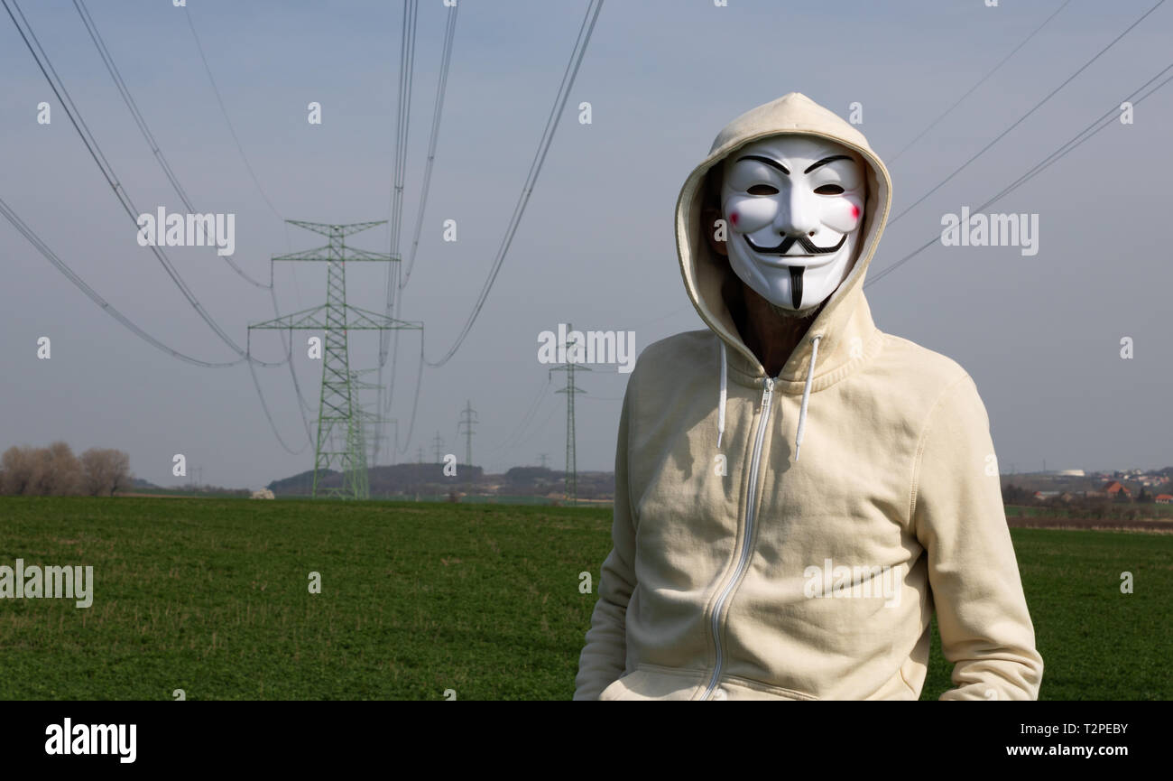Velvary, CZECH REPUBLIC – February 27, 2019: Man is wearing the Vendetta mask and standing on green field with electric pylon Stock Photo