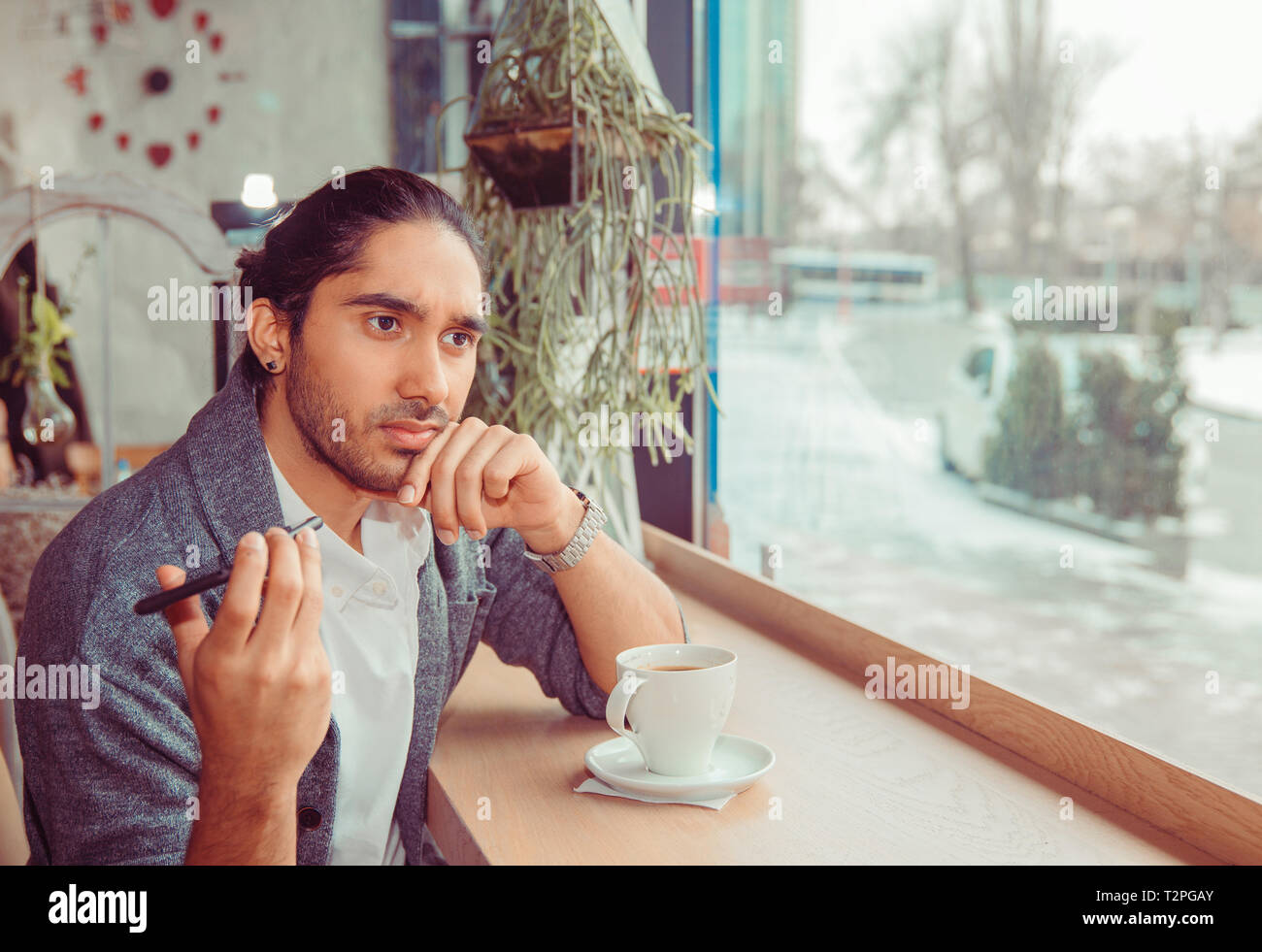 Upset man holding phone to the side, not listening to conversation, uninterested, having a fight by cell. Closeup portrait guy sitting near window at  Stock Photo