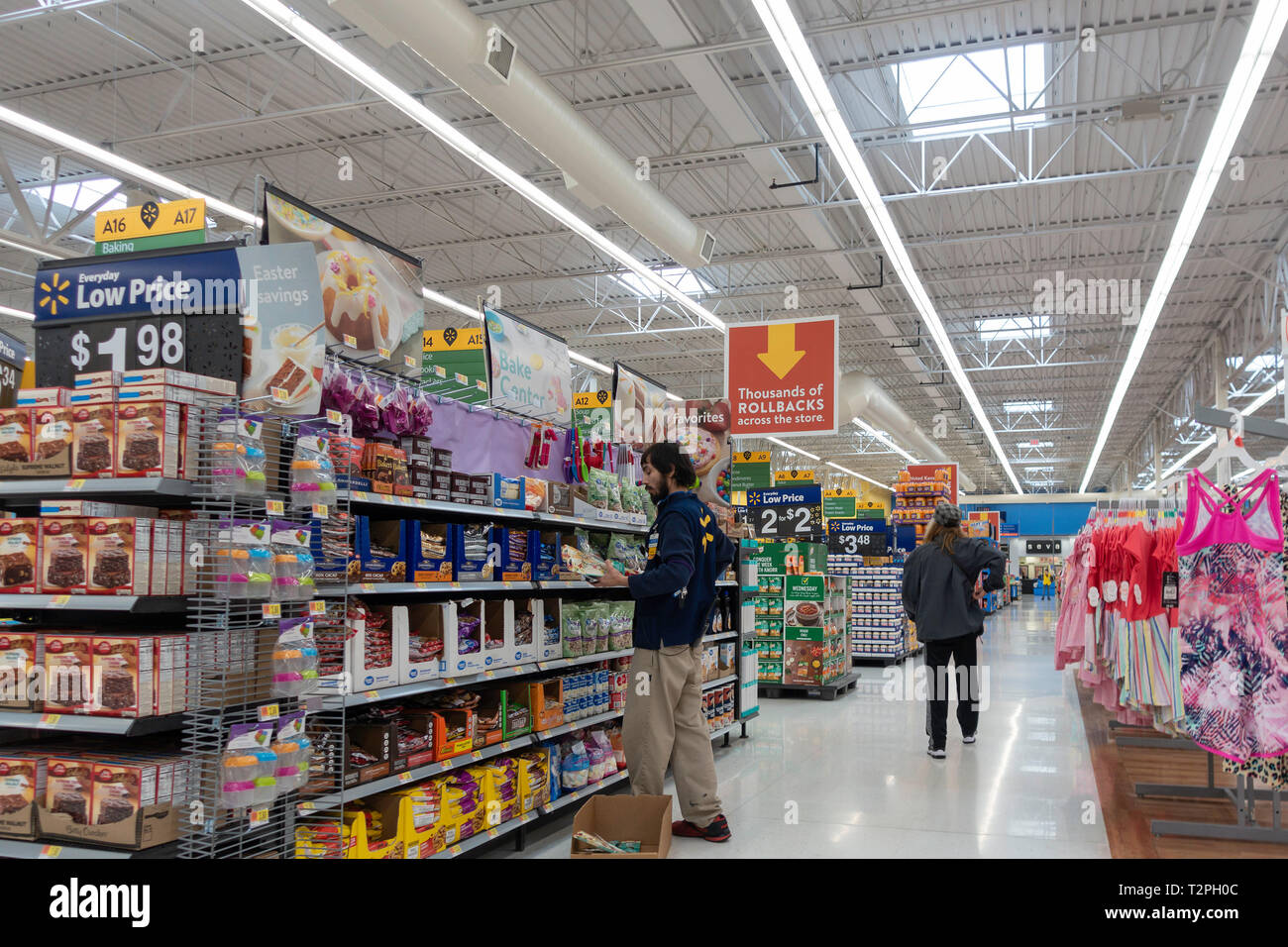 Walmart indoors with male employee stocking shelves while male customer walks down aisle. Stock Photo