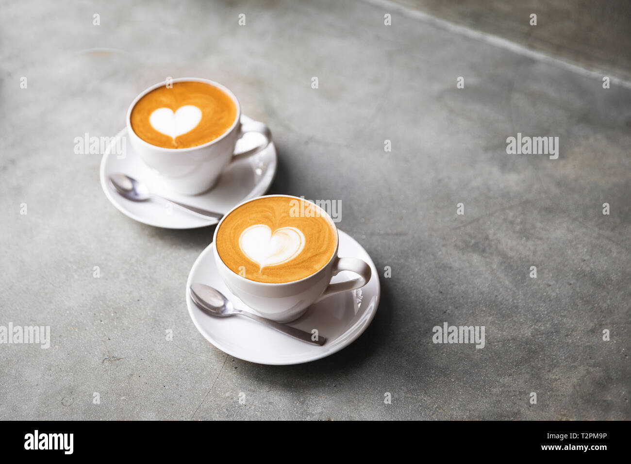Two white cups of tasty cappucino with love art latte. Valentine's concept. Concrete grey backdrop. Stock Photo