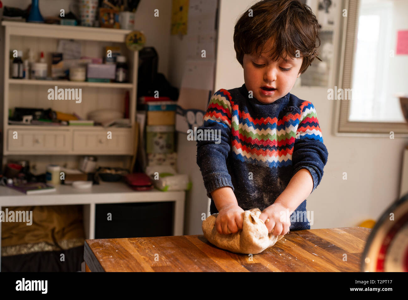 Toddler kneading dough on kitchen worktop Stock Photo