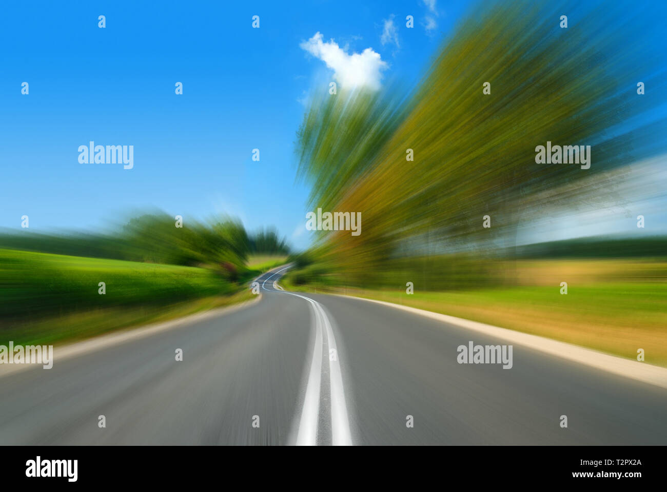Road among green fields with motion blur effect, blue sky in the background Stock Photo