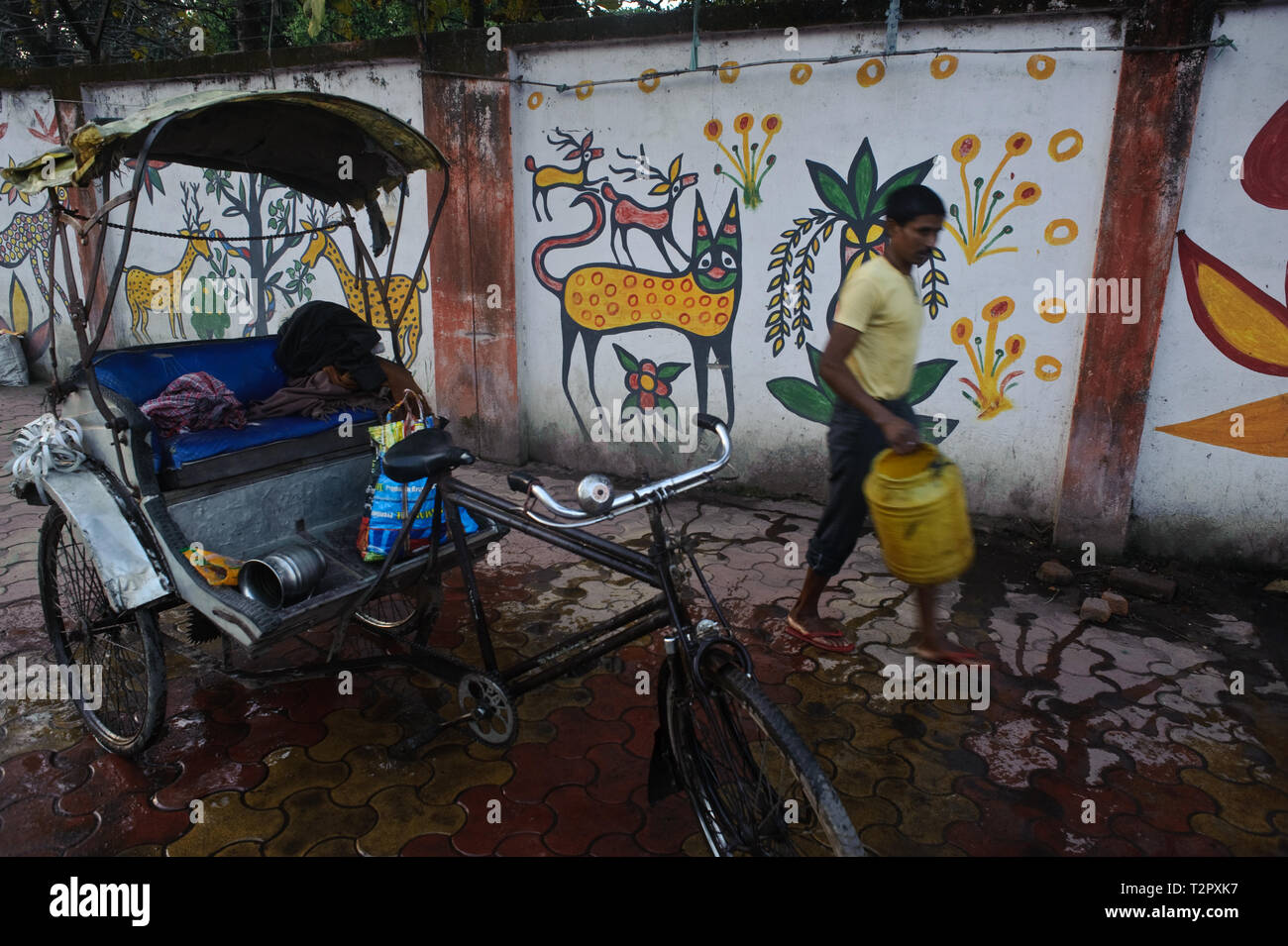 Cycle rickshaw puller washing his cycle rickshaw + mural painting inspired by local Sohrai art ( India) Stock Photo