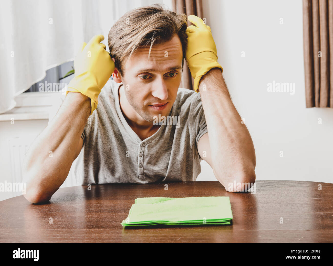 Dismay man with rubber gloves cleaning house. Housekeeper concept. Stock Photo