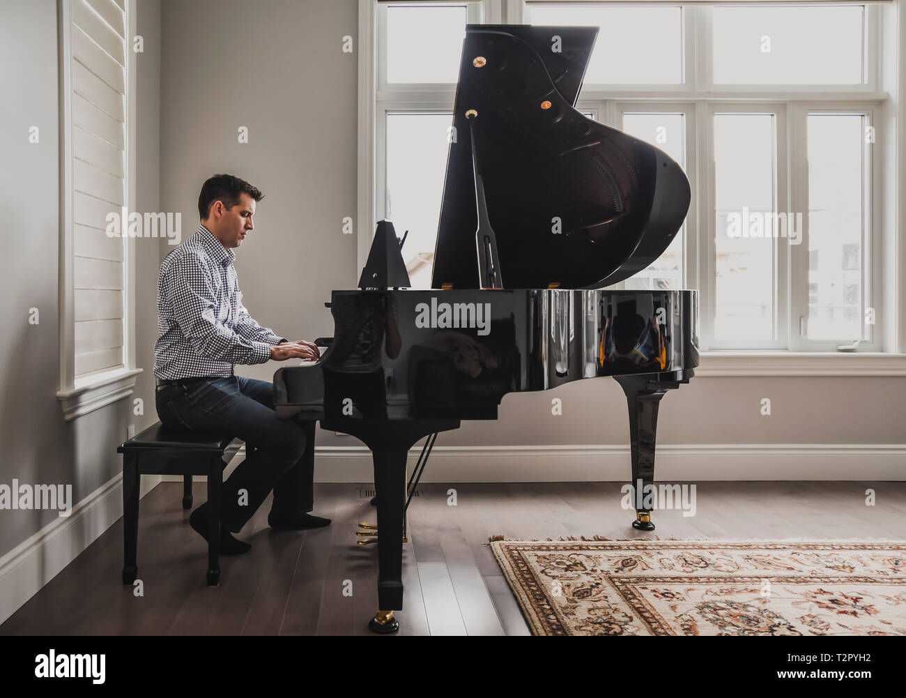 Man playing baby grand piano in a bright room Stock Photo