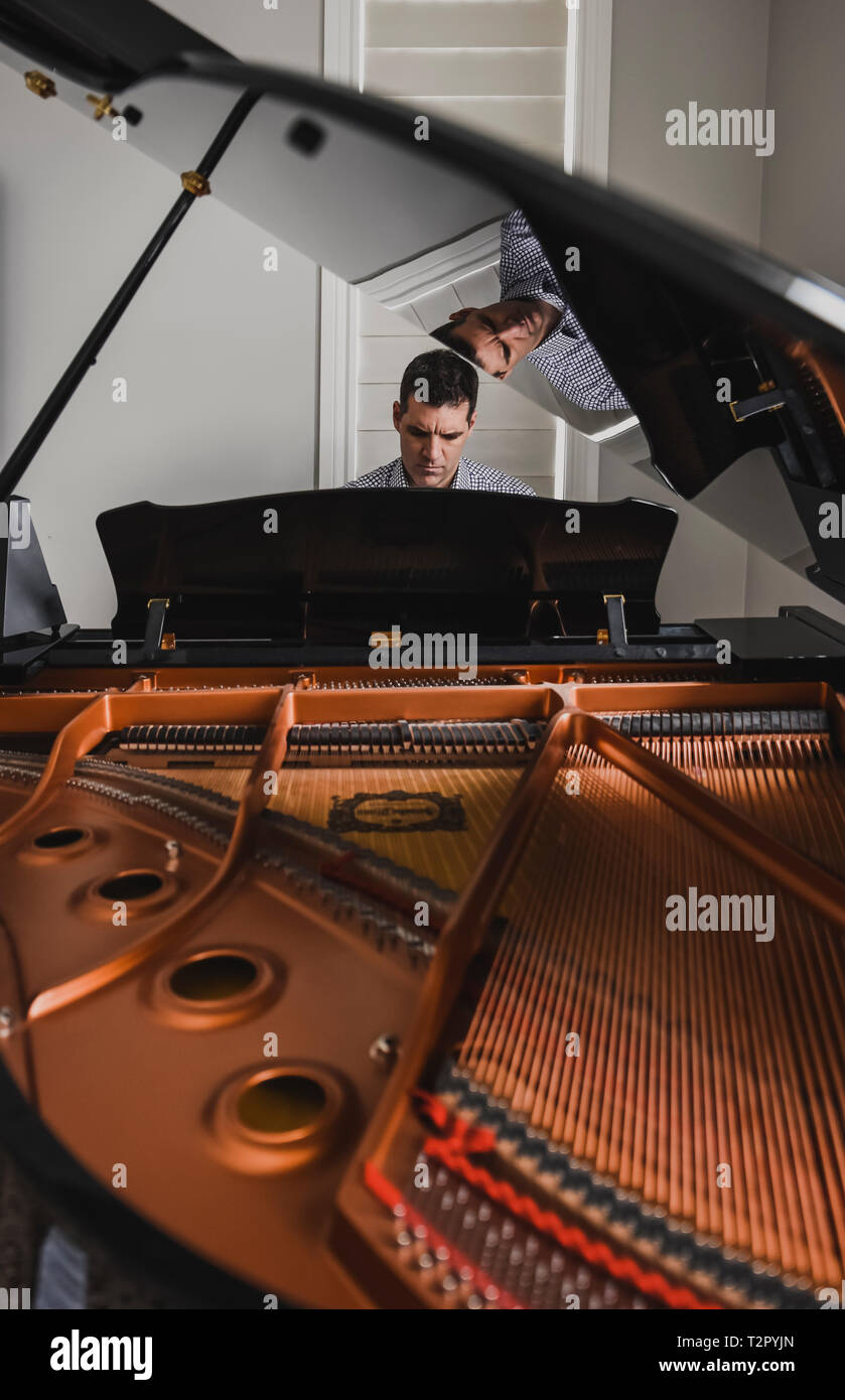 Man playing baby grand piano with inside of piano in foreground Stock Photo