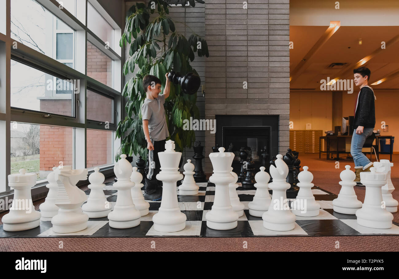 Two young boys playing chess with giant pieces in library Stock Photo