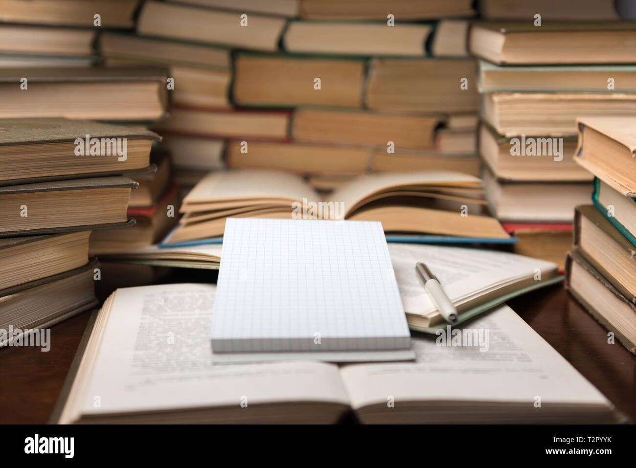 https://c8.alamy.com/comp/T2PYYK/education-learning-concept-with-open-book-and-notebook-on-the-table-stack-piles-of-books-on-reading-desk-and-glasses-in-bookshelves-background-T2PYYK.jpg