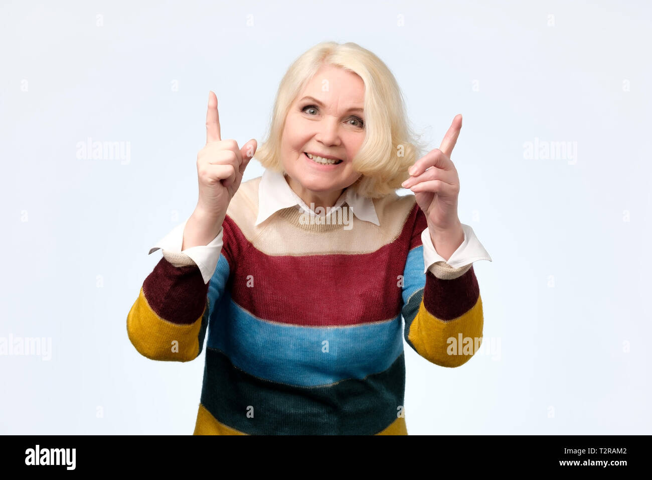 Pleased senior woman in yellow clothes warning you giving advice. Studio shot, isolated on gray background Stock Photo
