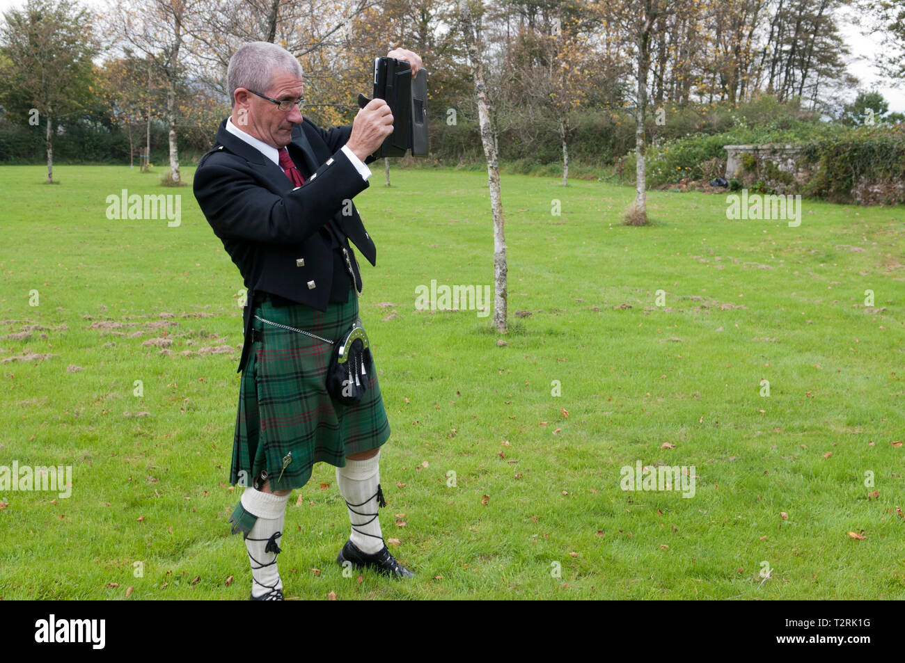 Man wearing a kilt, taking a photograph with his tablet Stock Photo