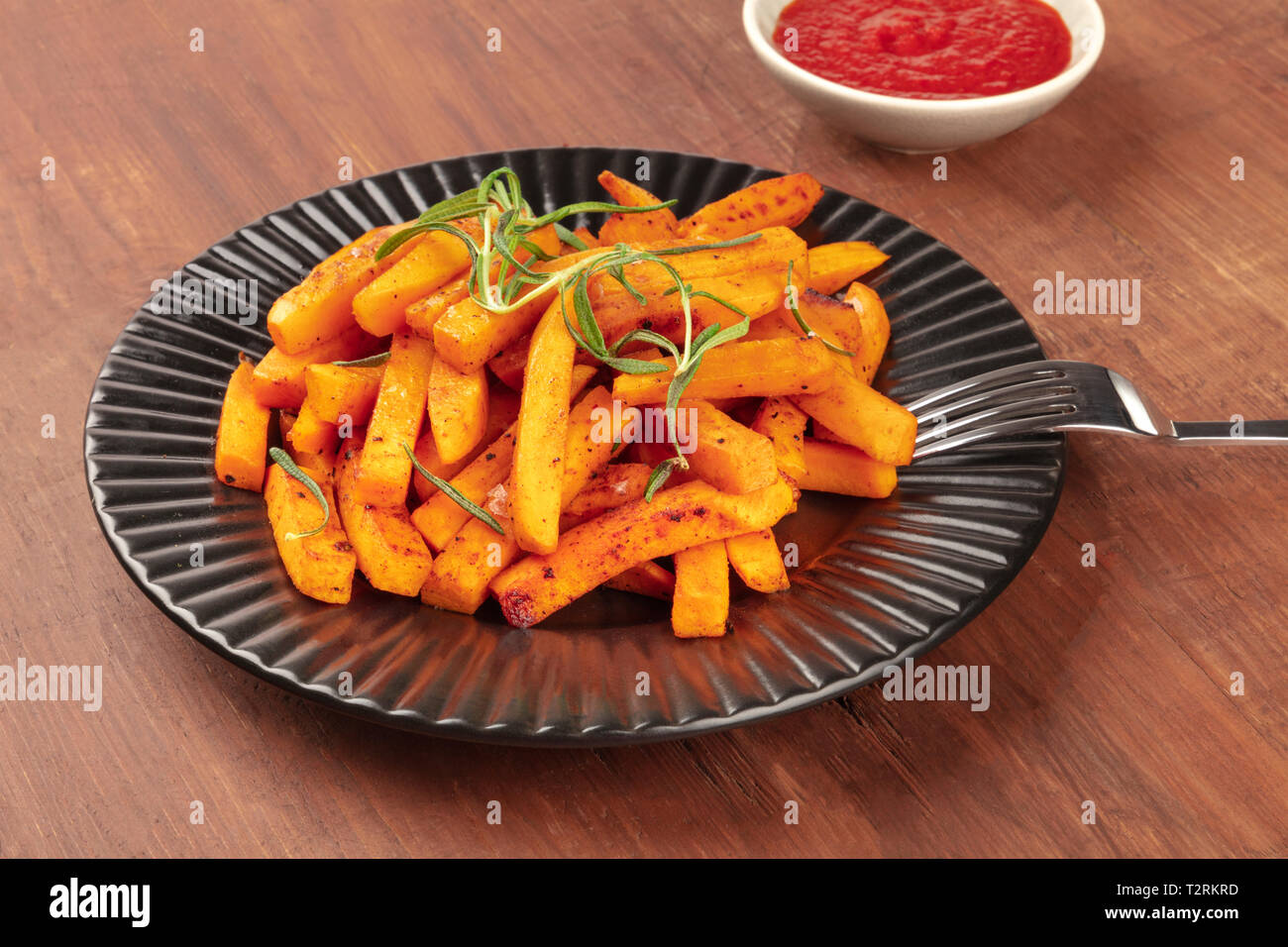 Roasted sweet potato fries with rosemary and tomato sauce on a dark rustic wooden background with a place for text Stock Photo