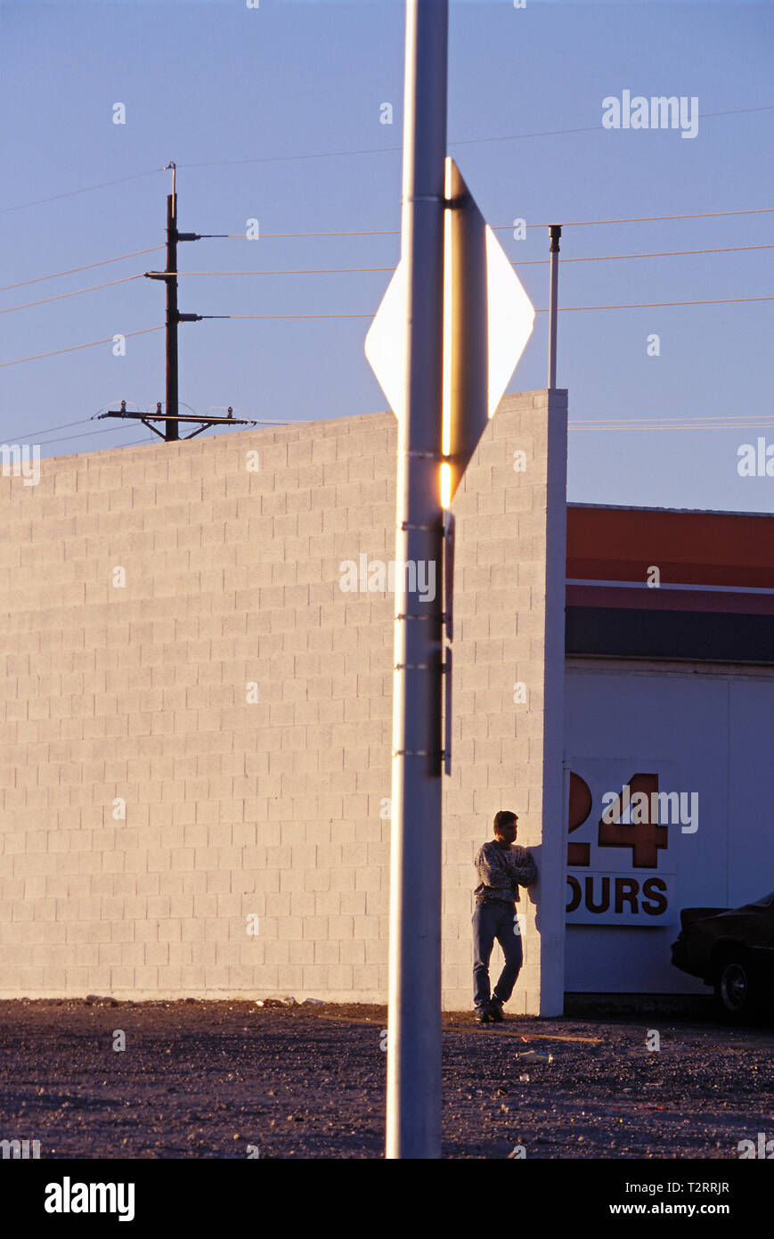 Man alone waiting in a vacant lot along side a very tall concrete wall Stock Photo