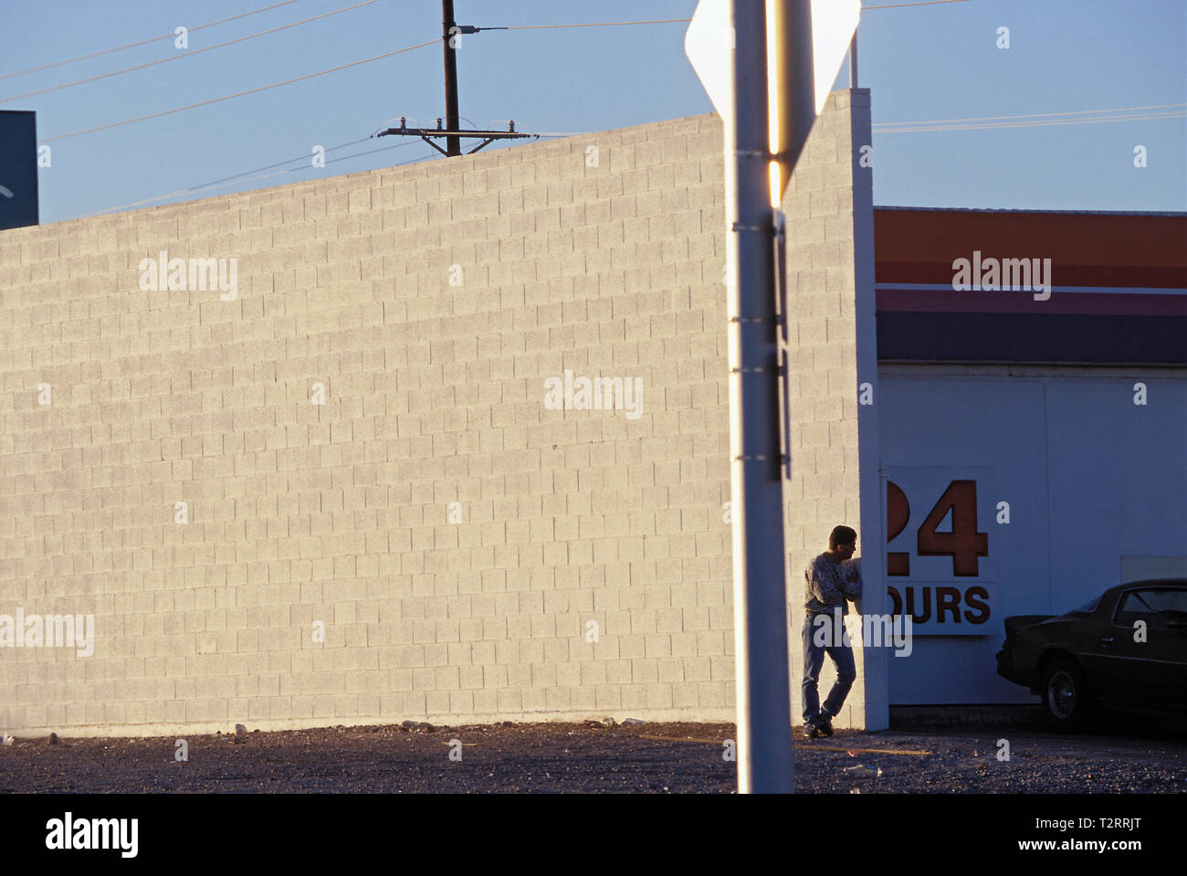 Man alone waiting in a vacant lot next to a very tall concrete wall Stock Photo