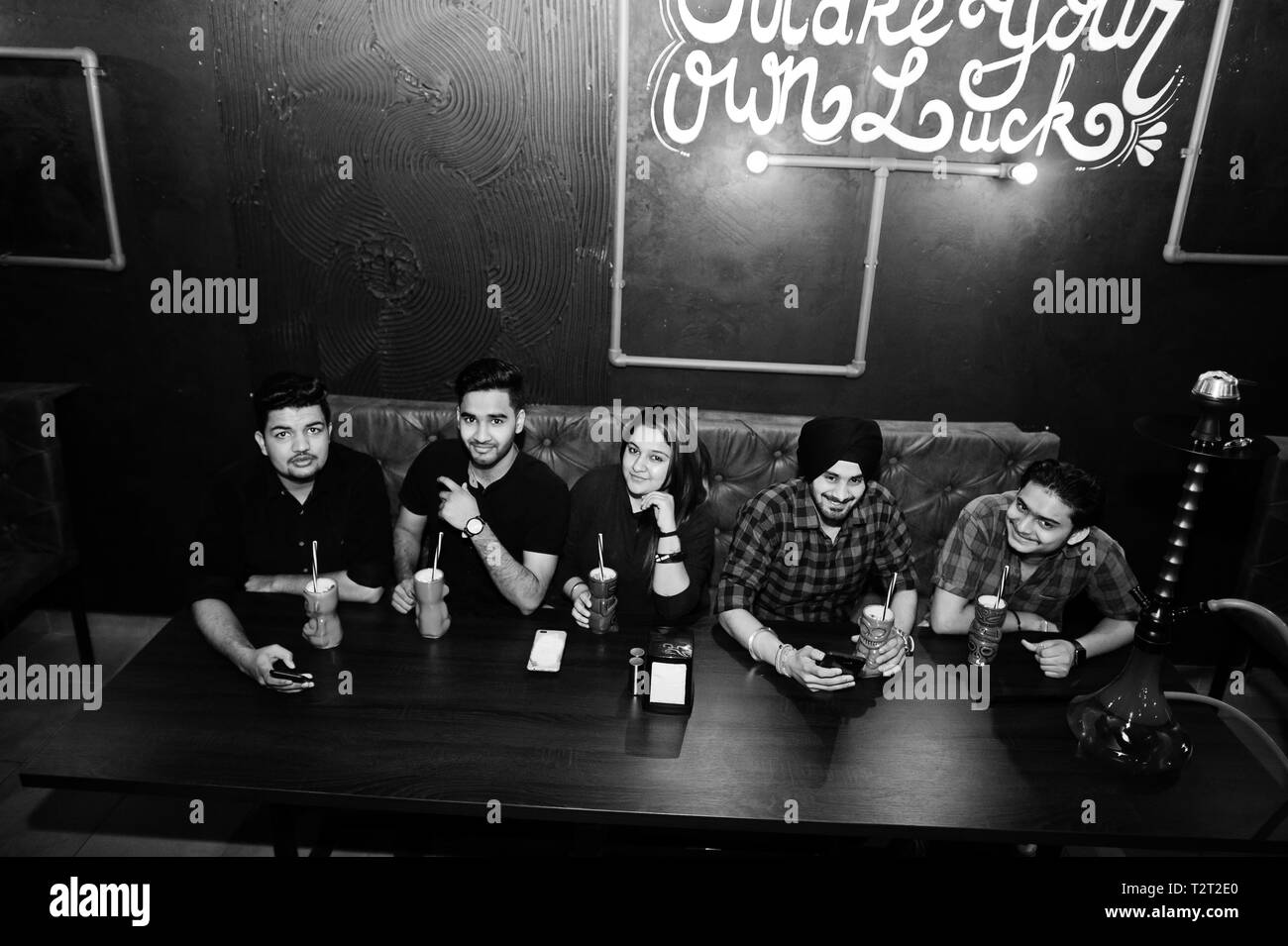 Make your own luck! Group of indian friends having fun and rest at night club, drinking cocktails and smoke hookah. Stock Photo