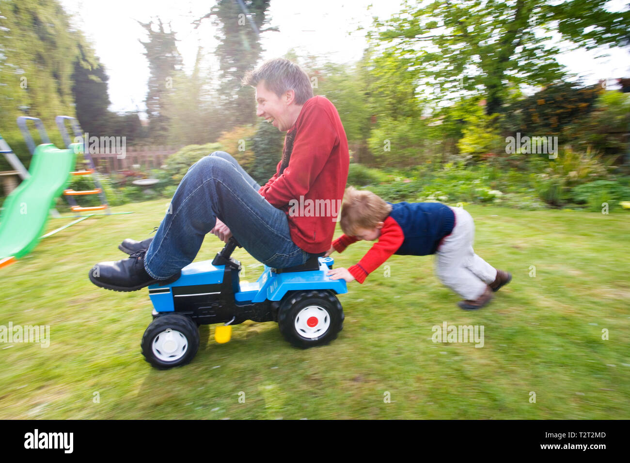 Father pushing his son on a toy tractor in their back garden Stock Photo