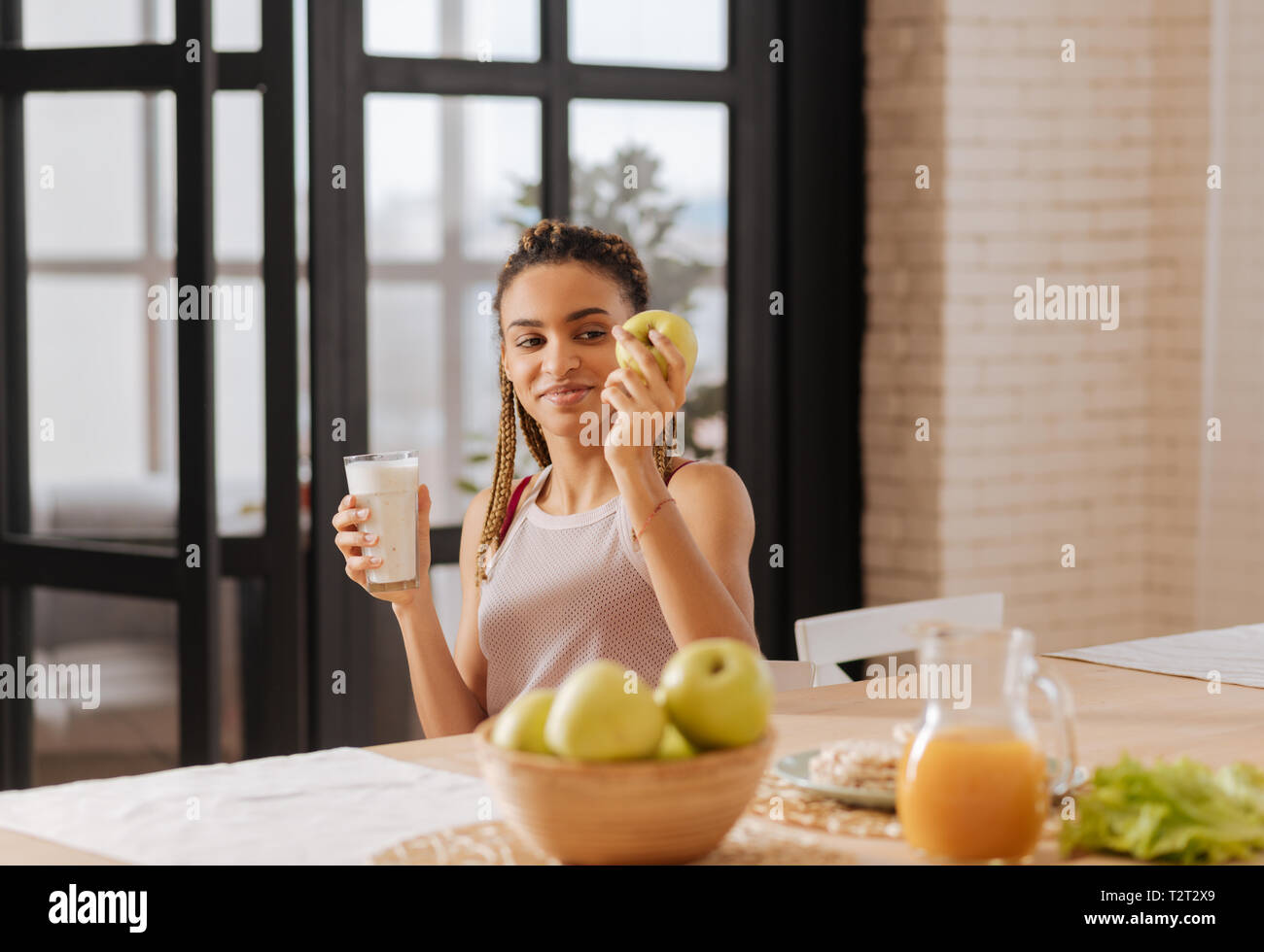 Eating apple. Dark-eyed appealing woman having healthy diet eating apple and drinking milk Stock Photo