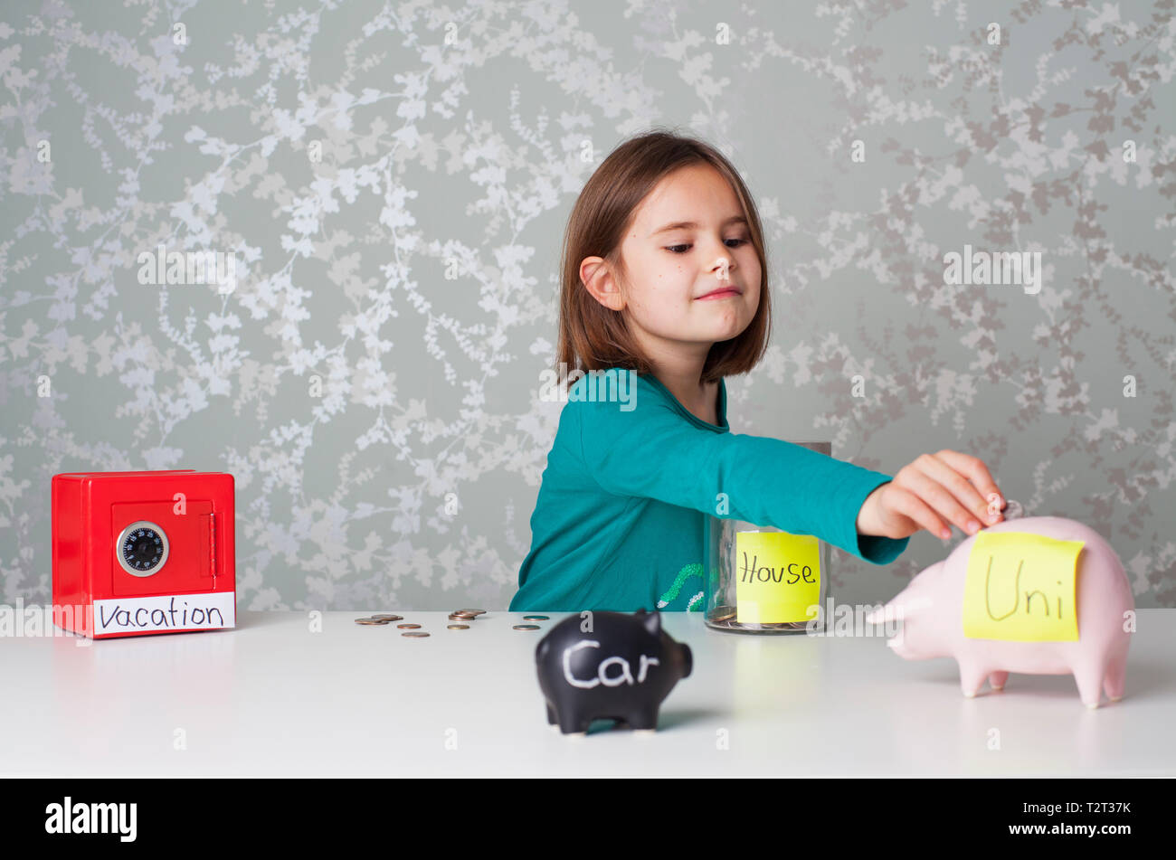 Young girl putting money into into different money boxes Stock Photo