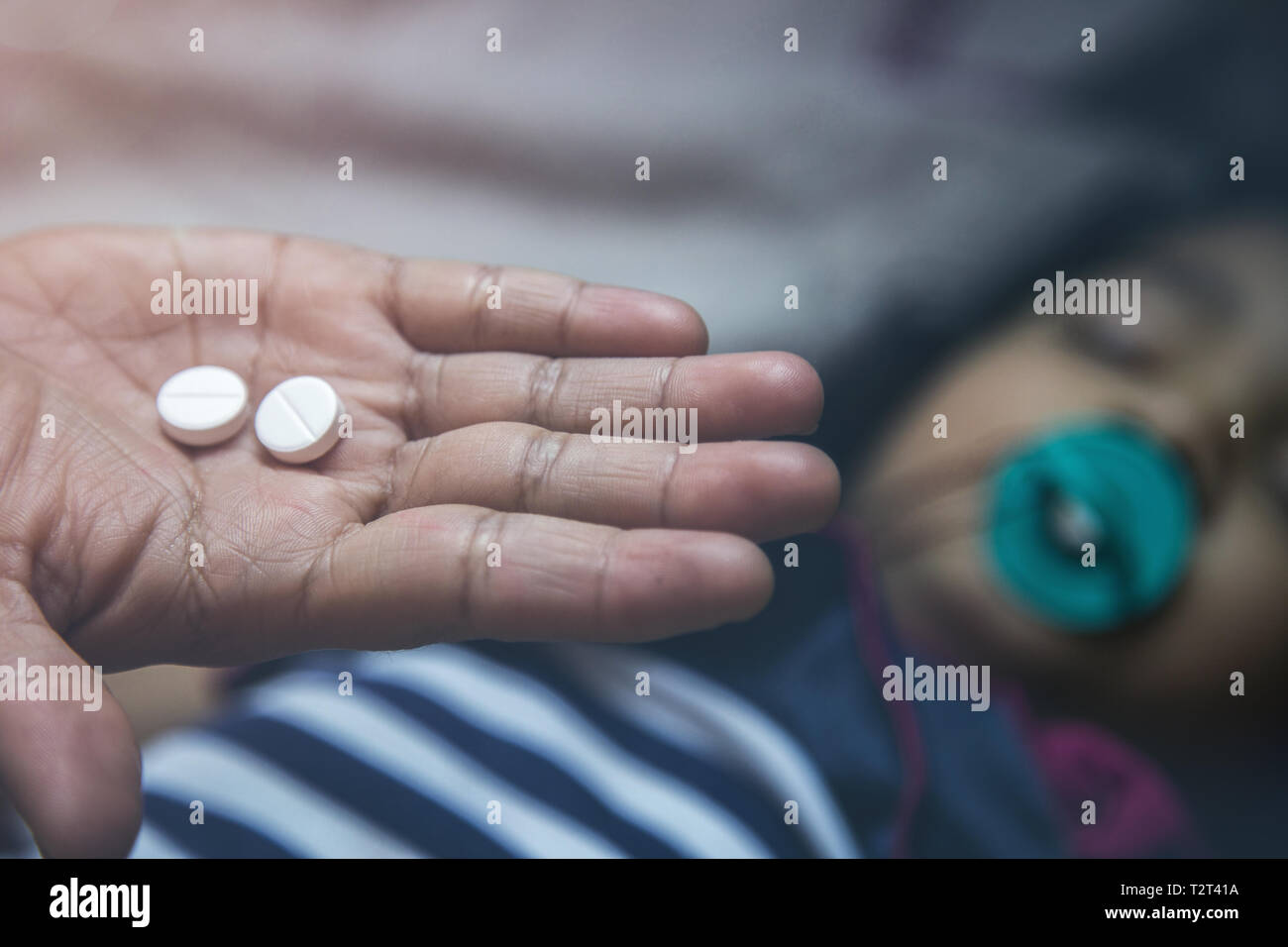 Close up of hand holding medicine pills over blurry illness Asian kid with pacifier in her mouth Stock Photo