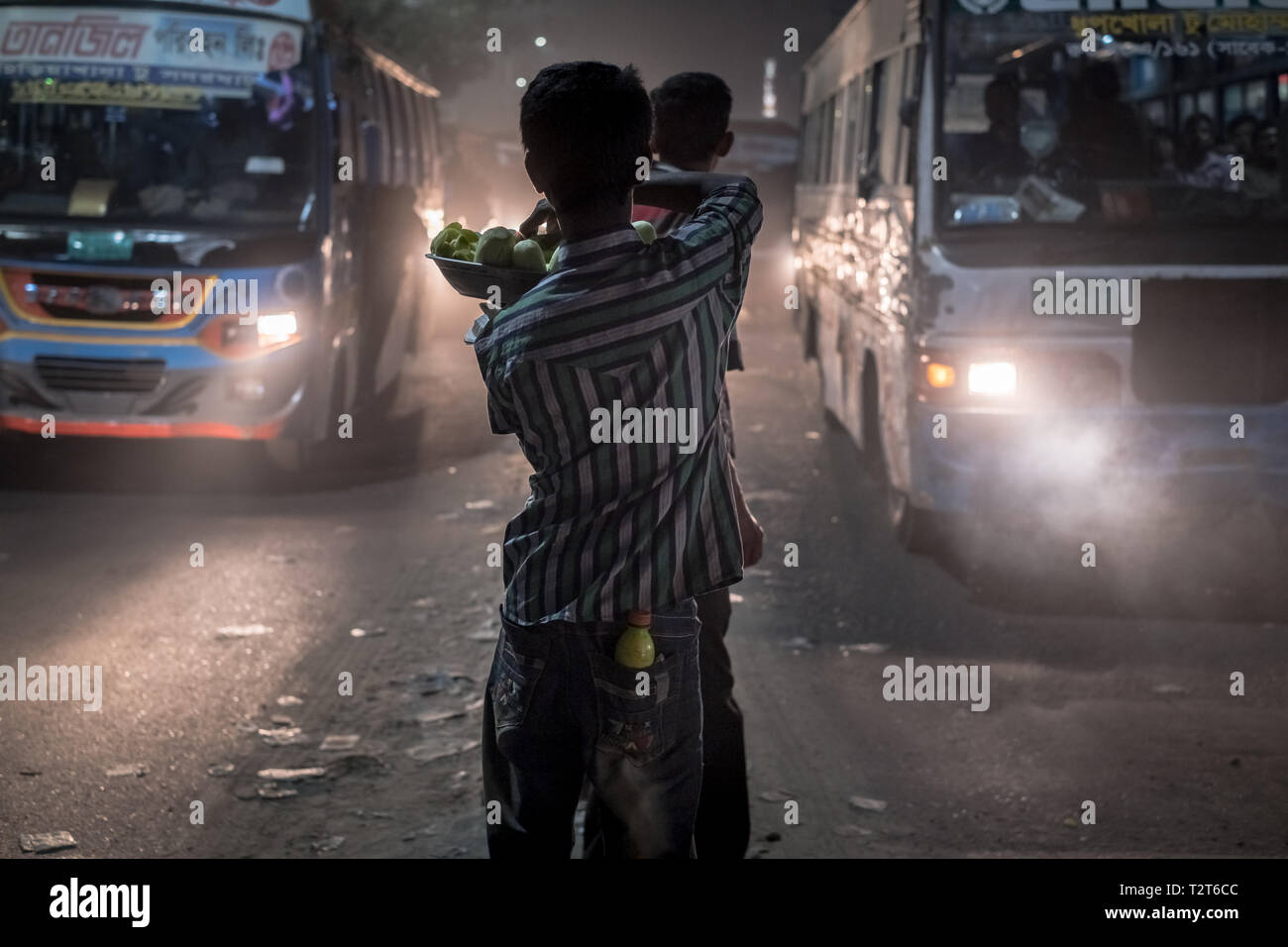 Street vendor selling vegetables in traffic jam in Dhaka, Bangladesh. Smog and air pollution is visible there day and night. Many buses around. Stock Photo