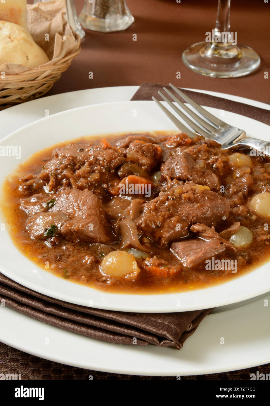 a plate of Boeuf Bourguignon with a basket of dinner rolls Stock Photo