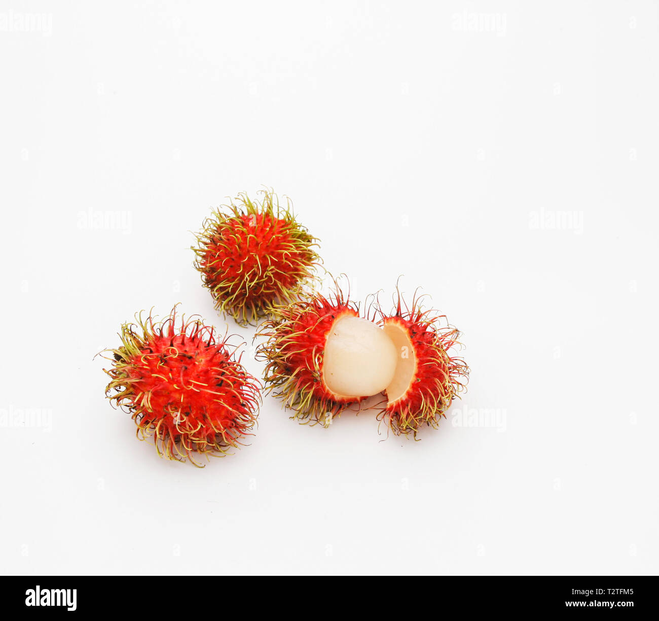 Three rambutans, one open. Delicious asian sweet fruit tasting a bit like lychee. The name rambutan is derived from the Malay word “rambut” meaning ha Stock Photo