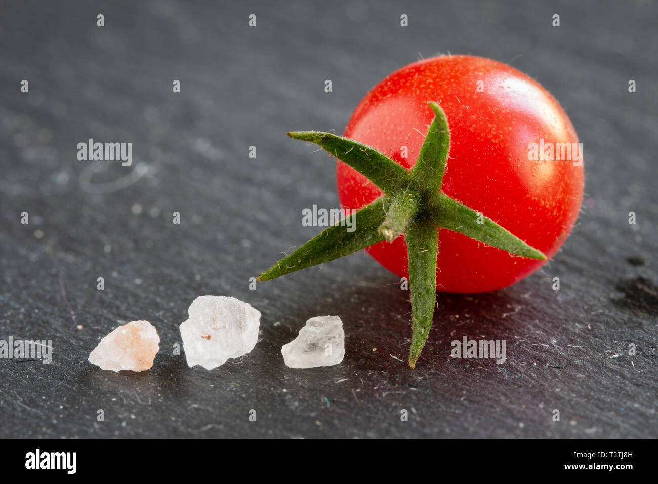 fresh wild currant tomato closeup isolated on a slate plate with copy space and salt crystals Stock Photo