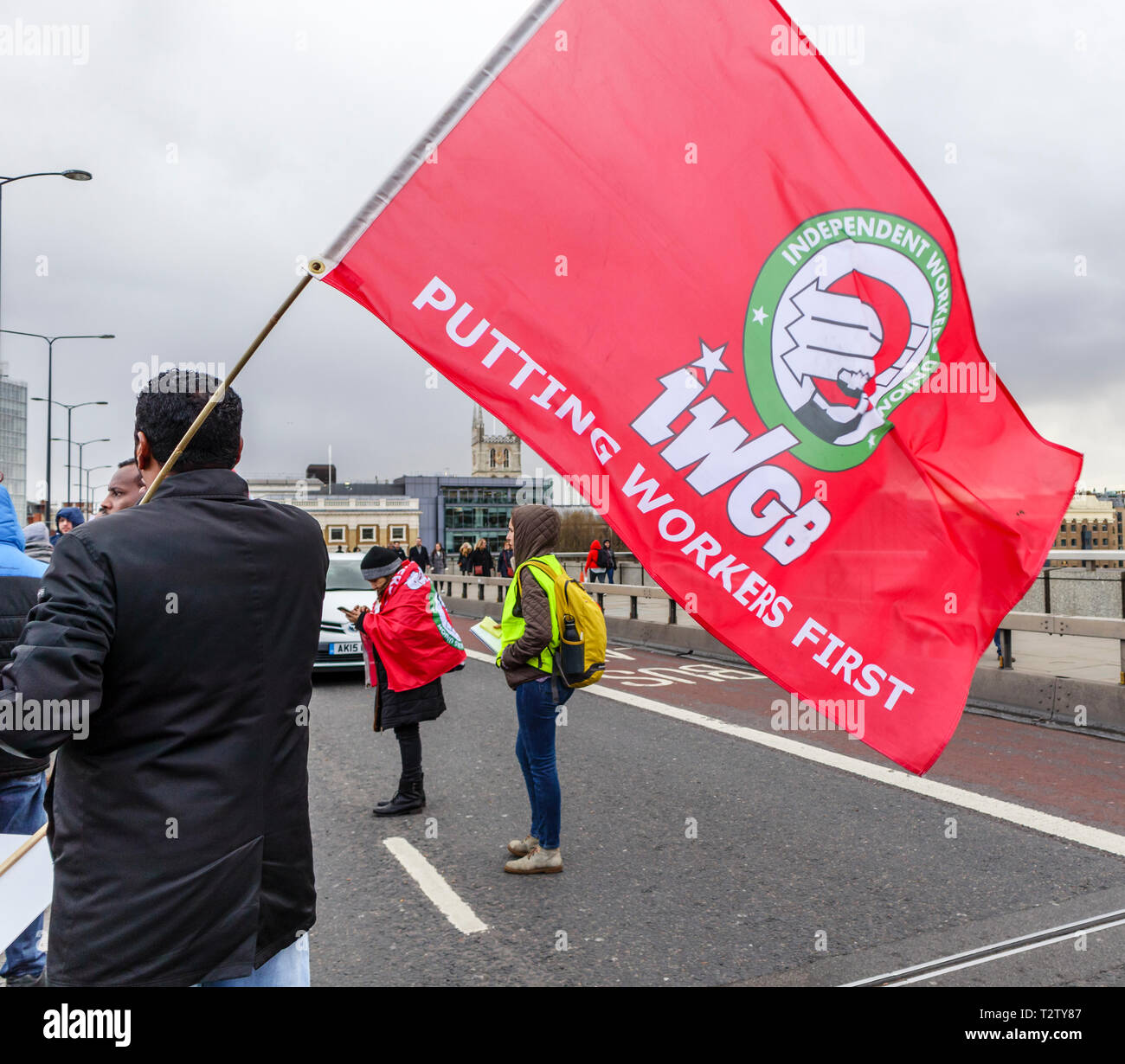 London, UK, 04th April 2019. Minicab drivers block the road on London Bridge protesting against the congestion change on private hire minicabs.  This demonstrators holds and waves the red flag of IWGB (Independent Workers Union of Great Britain). Credit: Graham Prentice/Alamy Live News Stock Photo