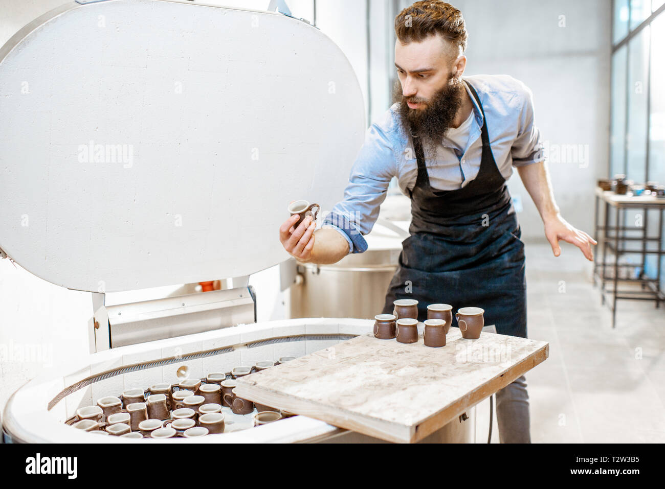 Man taking baked ceramic cups from the electric oven at the pottery