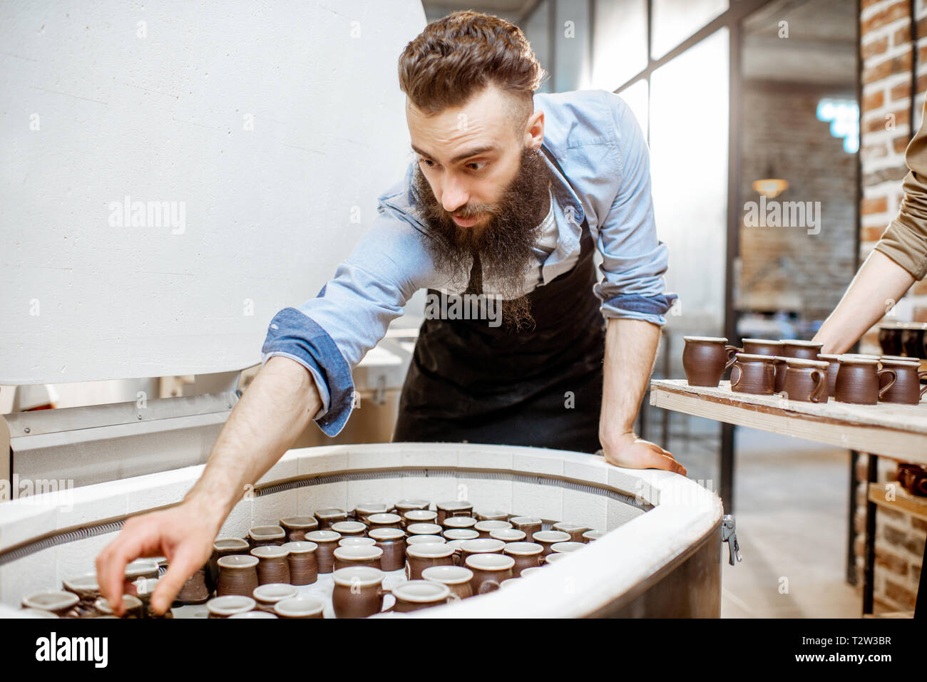 Man taking baked ceramic cups from the electric oven at the pottery