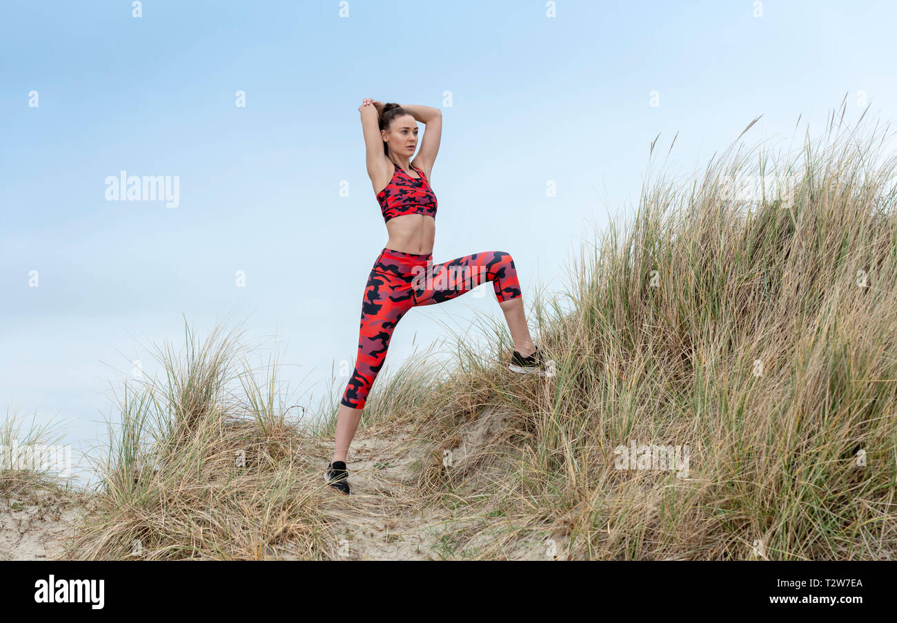woman doing warm-up stretching exercises outside in the sand dunes, wearing colourful sportswear Stock Photo