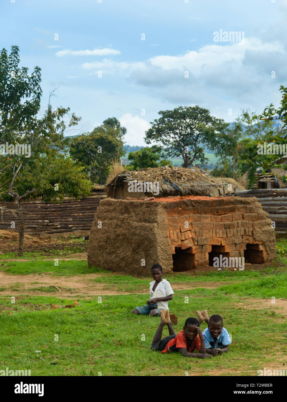 children lie on the ground in front of a small brick kiln in a Malawian village Stock Photo