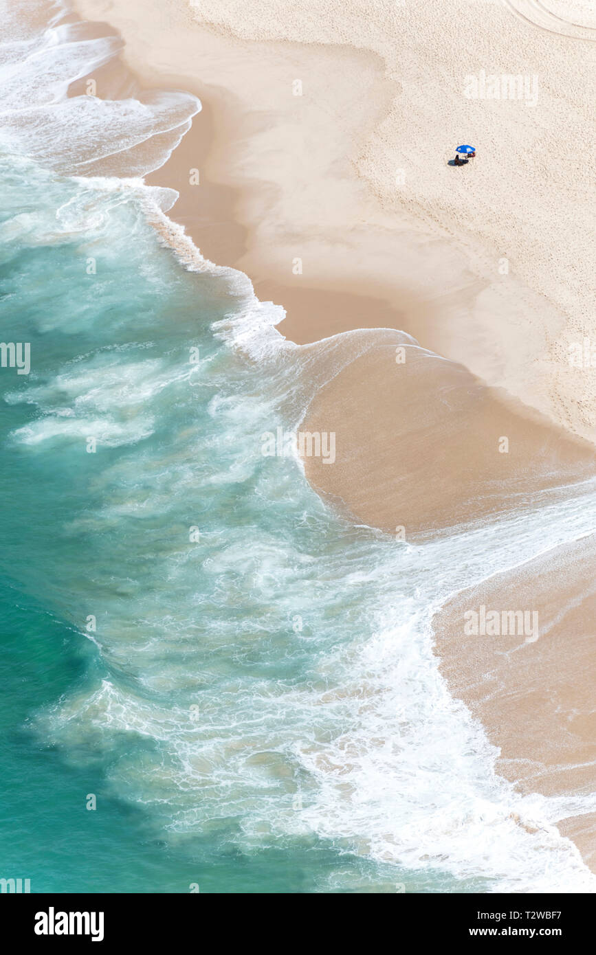 Aerial photograph of a blue water beach with waves spreading in the sand and a tent on the beach. Stock Photo