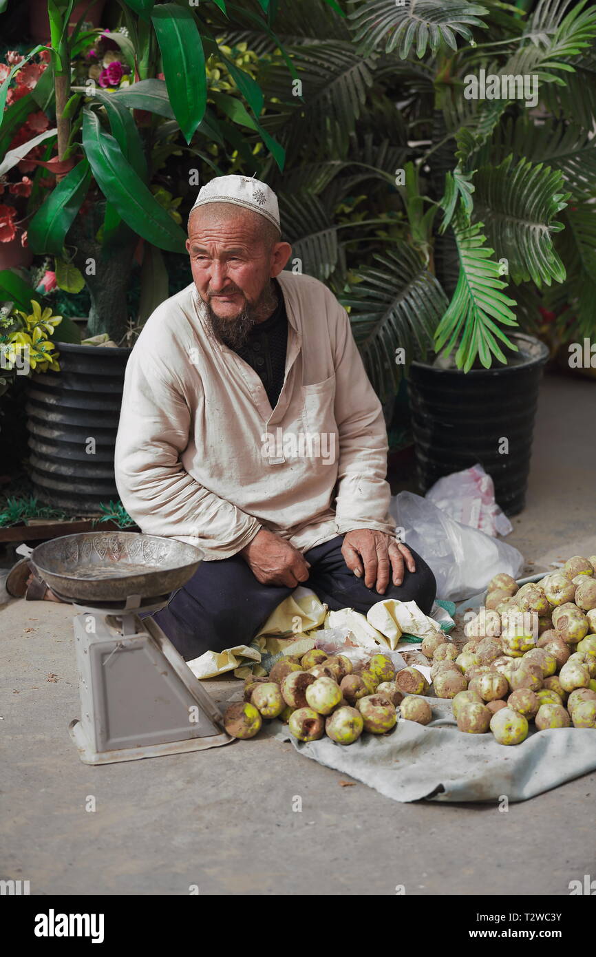 Doppa skullcapped-bearded Uyghur man sells bruised green apples. Hotan's Bazaar-Xinjiang-China-0079 Stock Photo